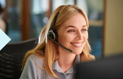 Smiling woman wearing a headset, sitting at a desk with a computer.